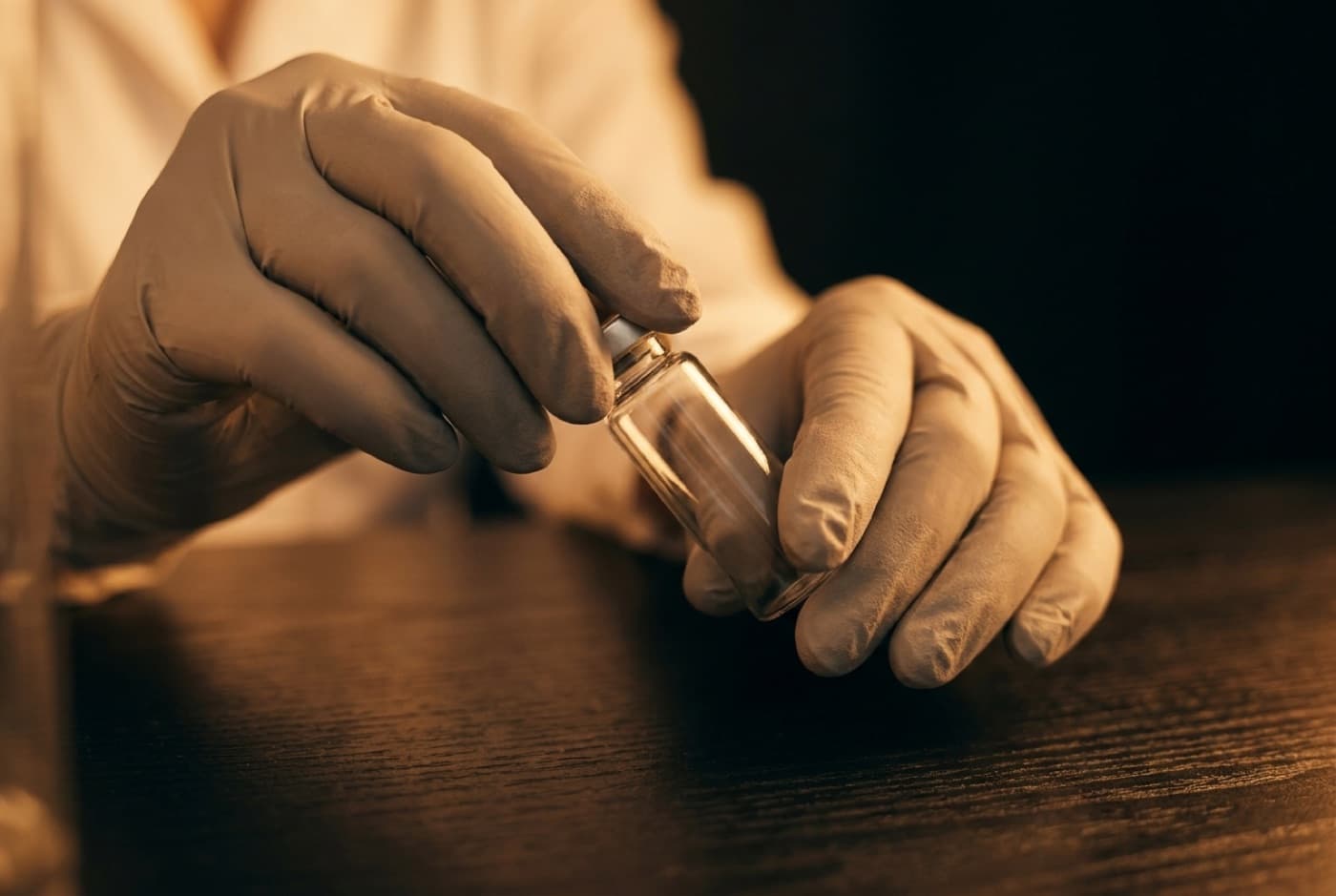 Gloved hands holding a sealed vial at a laboratory bench